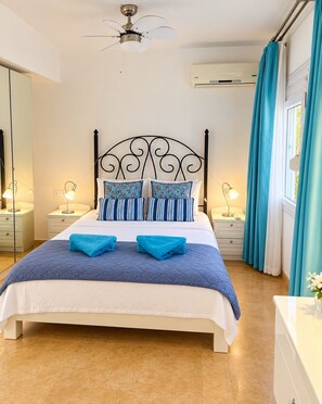 A neatly made bed with a headboard, two bedside lamps, and a ceiling fan.