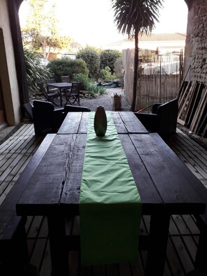 Een houten patio tafel met een groene tafelkleed, omringd door rieten stoelen.