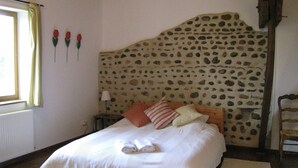 A bedroom with a stone headboard, a bed with white bedding, two pillows, and a nightstand with a lamp. - Peaceful private base in Pyrenees, large pool, perfect for outdoor enthusiasts (Thuy)