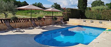 A swimming pool with lounge chairs and umbrellas, surrounded by stone walls and greenery.