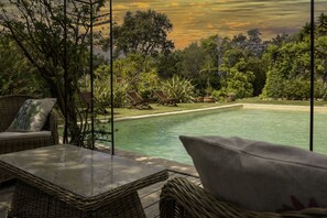 Ein Außenbereich mit Korbmöbeln und Blick auf einen Pool, der von üppigem Grün umgeben ist.