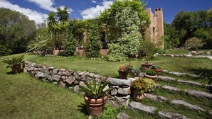 A garden with a stone wall, potted plants, and a building with a tower. - Pinarello: CHARMING HOUSE 400m FROM THE BEACH, SWIMMING POOL AND SPA (Zonza)