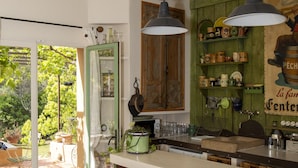 A kitchen with a bar area, stools, hanging lights, and a view of the garden. - Pinarello: CHARMING HOUSE 400m FROM THE BEACH, SWIMMING POOL AND SPA (Zonza)