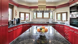 A spacious kitchen with red cabinetry, a central island with fruit, and a large range hood. - Acharavi Beach Villa - Luxury Seaside Villa Rental in Acharavi, Island of Corfu. (Acharavi)