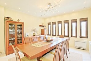 Une salle à manger avec une longue table en bois, des chaises, un lustre et un buffet aux portes vitrées.