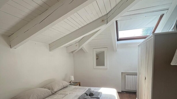 A bedroom with a sloped ceiling, a bed with a lace bedspread, a nightstand, and a wardrobe. - 5 MINUTES FROM THE S. LUCIA TRAIN STATION (Venezia)