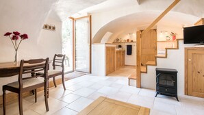 Un coin repas avec une table et des chaises en bois, une cuisine avec des meubles et un fourneau en bois, et un escalier menant à un autre niveau.