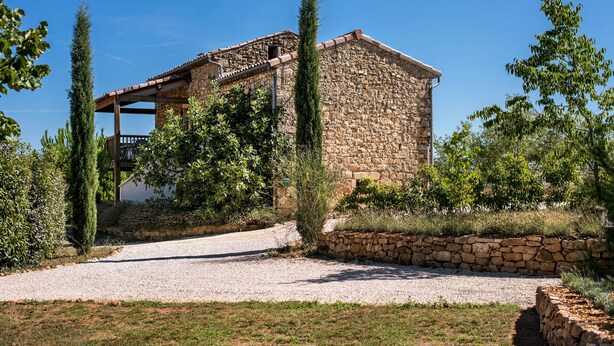 Un bâtiment en pierre doté d’un porche couvert et d’une allée gravillonnée.