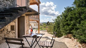 Un espace extérieur aménagé avec une table et des chaises, un bâtiment en pierre et une vue sur un paysage boisé.