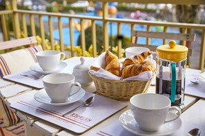 Un plateau de petit-déjeuner avec des croissants, du café et du thé, disposé sur une table offrant une vue sur une piscine.