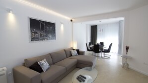 Ein modernes Wohnzimmer mit einer Eckcouch, einem Glastisch und einem Essbereich mit einer Kronleuchter.