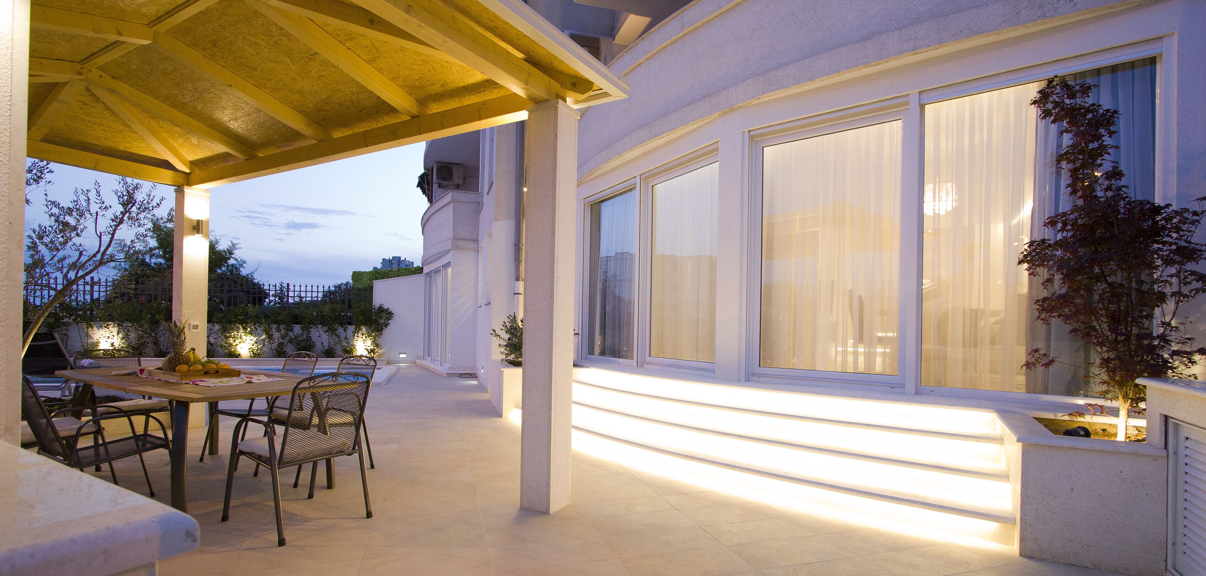 An outdoor patio with a table and chairs, large windows, and a covered area.