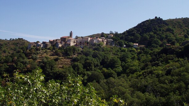 Un village perché sur une colline, avec des bâtiments traditionnels, une végétation luxuriante et un ciel dégagé.