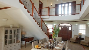 A spacious dining area with a high ceiling, a staircase, and a large wooden door. - 4 Bed Colonial Style Villa with pool in private setting, short walk to 2 beaches (Gibbes)