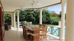 A covered patio with a dining table set for six, surrounded by wooden chairs. - 4 Bed Colonial Style Villa with pool in private setting, short walk to 2 beaches (Gibbes)
