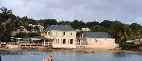A coastal building with a balcony overlooking the sea, a person in a yellow kayak, and palm trees in the background.