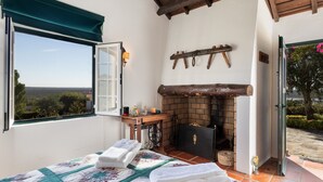 A bedroom with a bed, a fireplace, a window with a view, and a door leading outside. - House Countryside with view on the Dam, with Pool, lawn, Barbecue, porch (Barragem de Montargil)