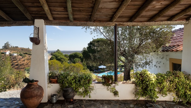 A covered patio with stone flooring, potted plants, and a view of a pool and hills in the background. - House Countryside with view on the Dam, with Pool, lawn, Barbecue, porch (Barragem de Montargil)