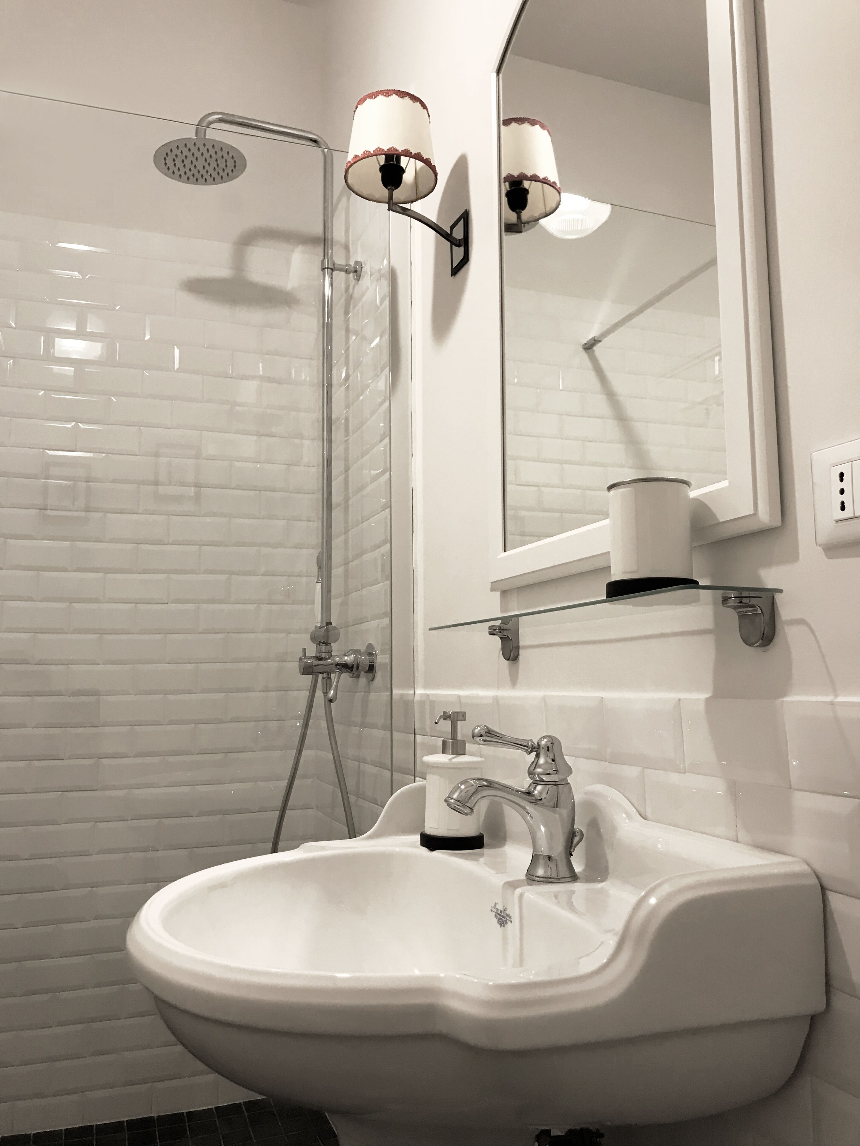 Une salle de bain avec un lavabo blanc, un miroir, une pomme de douche et un distributeur de serviettes.