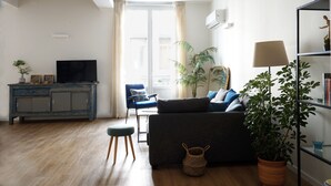 Una sala de estar con un sofá, un televisor sobre un mueble, una silla, una planta y una lámpara.