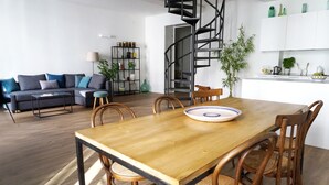 Una sala moderna con una mesa de comedor de madera, sillas de madera, un sofá, una estantería y una escalera de caracol.