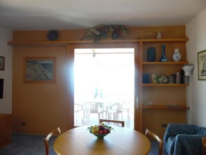 Een eetgedeelte met een ronde tafel, stoelen, een fruitschaal en een boekenkast met boeken en decoratieve objecten.