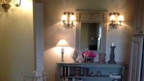 Een goed verlichte gang met een lamp, een spiegel en een boekenplank met boeken en decoratieve objecten.