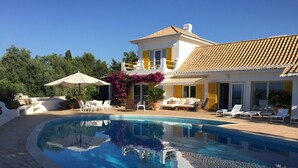 Una piscina con lettini e una casa con tetto in tegole.