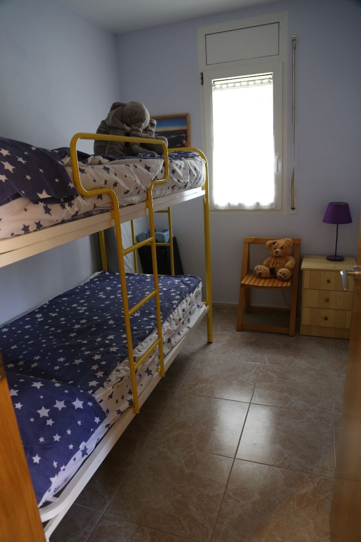 A bunk bed room with a window, a chair, and a small table.