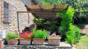 Un edificio in pietra con una parete in pietra rustica, una pergola in legno e vasi con fiori rossi.