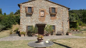 Un edificio in pietra con una porta centrale, due finestre con persiane e un piccolo portico con piante in vaso.