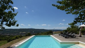 Una piscina rettangolare con bordo in pietra, circondata da sdraio e un pergolato.