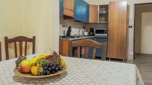 Uma mesa de jantar com uma cesta de frutas, uma cozinha com armários azuis, um micro-ondas e um fogão.