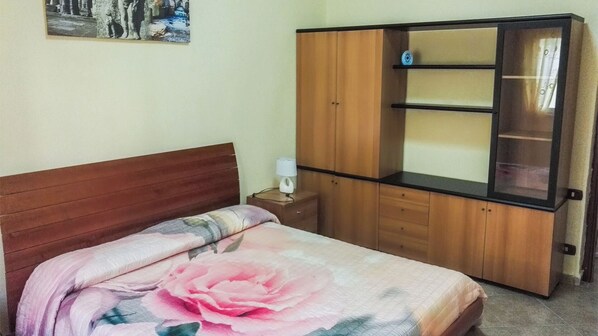 Un dormitorio con cama de madera, una mesita de noche con lámpara y un armario con espejo.