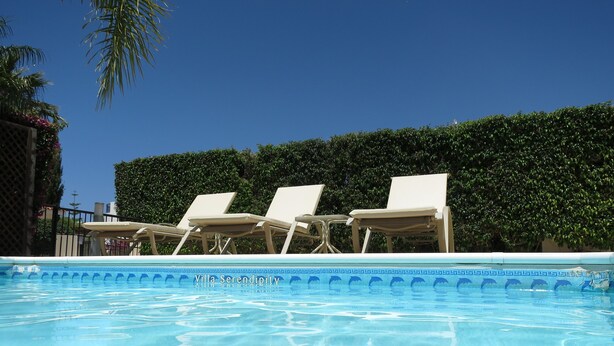 Una piscina azul cristalina con sillas de descanso y un seto al fondo.