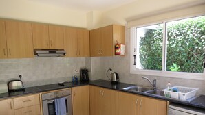 Una cocina moderna con armarios de madera, un lavamanos de acero inoxidable, lavavajillas y una ventana con vistas a zonas verdes.