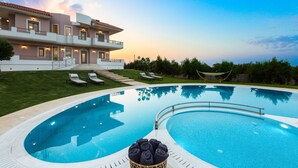 A modern hotel with a swimming pool, a well-maintained lawn, and a view of the sea at sunset. - Aelia Residence, Wellness & Leisure with 100m² Heated Pool, Whirlpool, Sauna&Gym (Rethymnon)