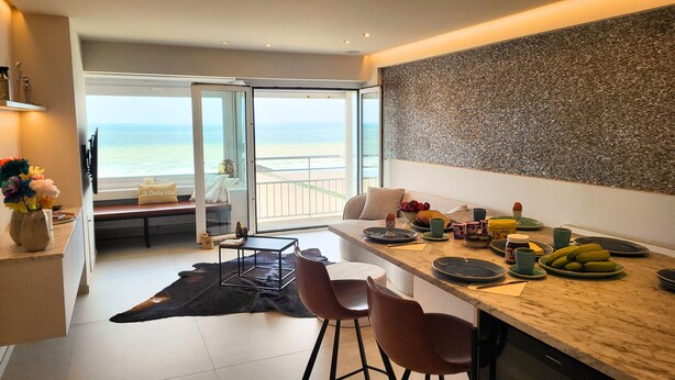 A modern kitchen with a view of the beach, a dining area with chairs, and a large window. - Maramar Westend Luxury Apartment with Sea View (Middelkerke)