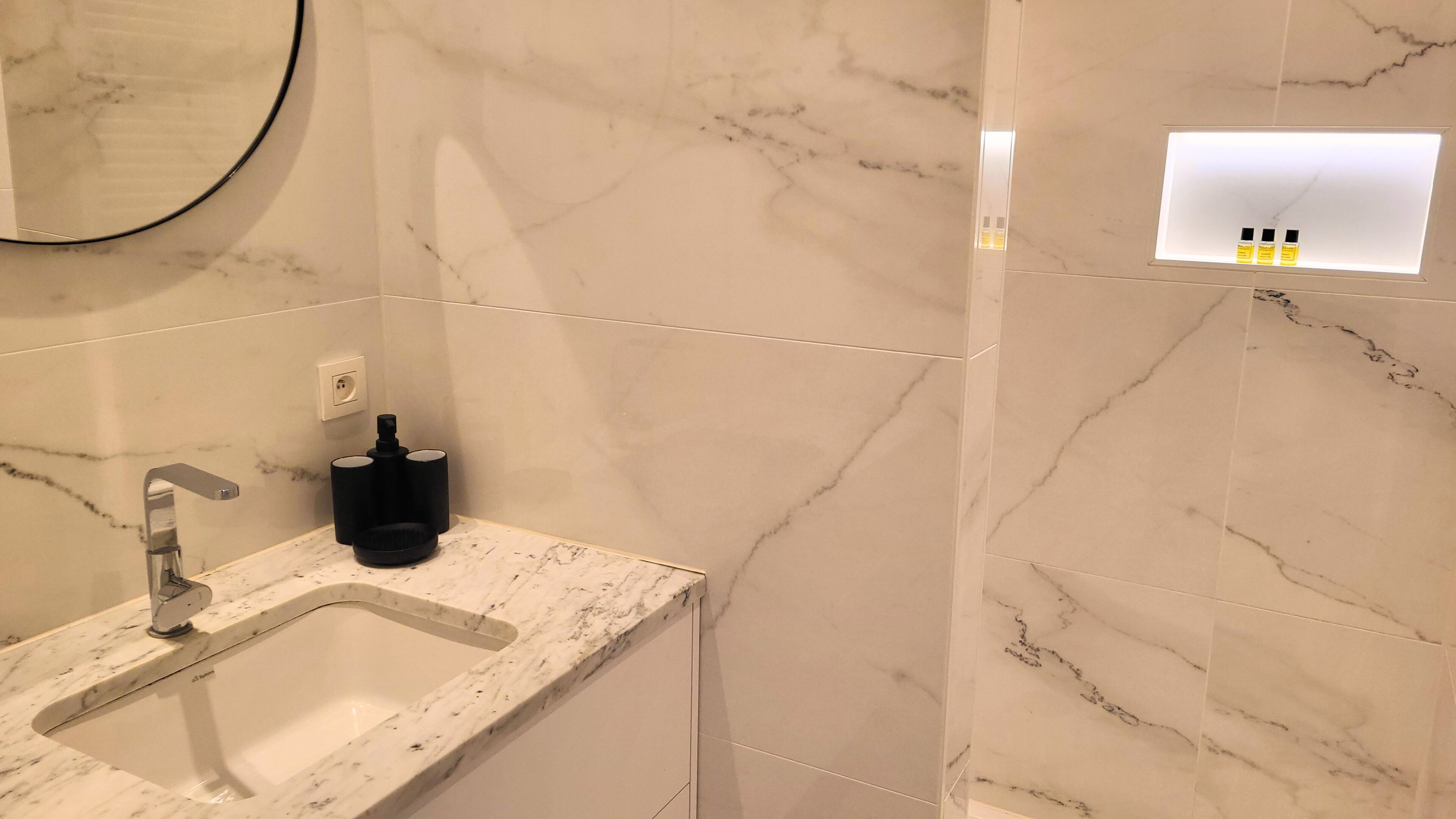 Un baño con lavamanos, espejo y dispensador de artículos de aseo.