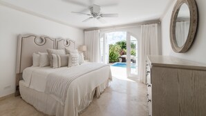 A bedroom with a bed, a ceiling fan, a large mirror, and a view of an outdoor pool. - Sugar Cane Ridge 23 (St James)