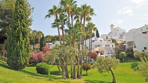 A coastal village with white buildings, palm trees, and a well-maintained grassy area.