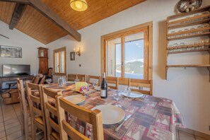 A dining area with a wooden table set for four, chairs, a clock, and a television in the background.