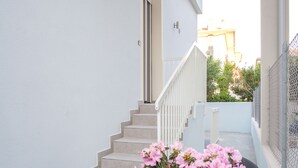 Un balcon avec une table et des chaises, un pot de fleurs orné de fleurs roses et un escalier menant à une porte.