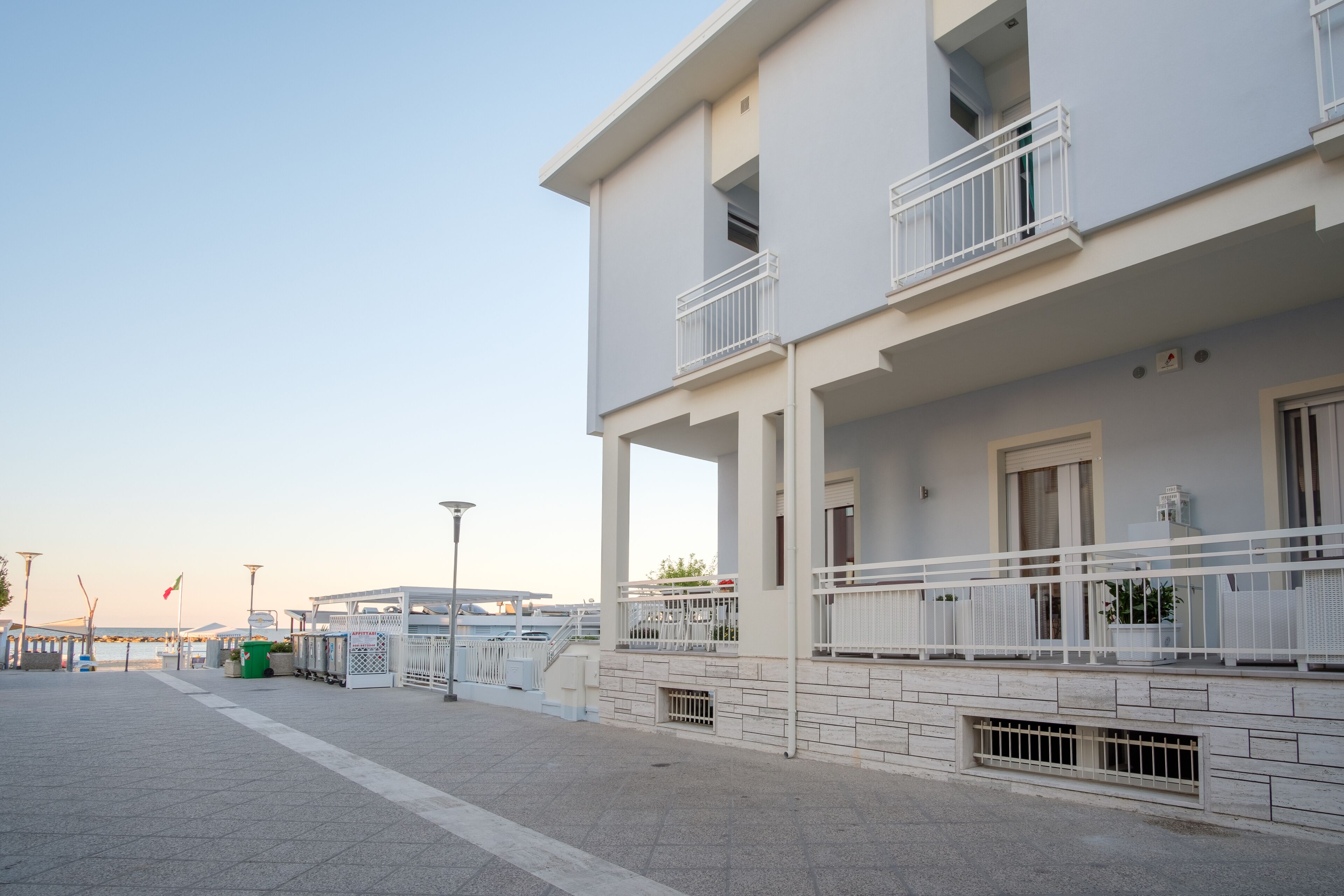 A two-story building with balconies, a paved walkway, and a clear sky.
