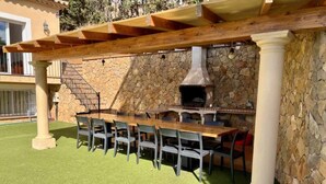 An outdoor patio with a stone wall, a wooden pergola, and a barbecue grill. - Mas Ambros House with infinity pool and barbecues in Calonge, Girona Costa Brava (Calonge)
