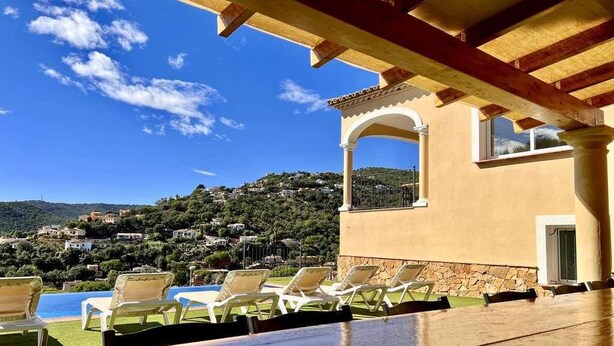 A terrace with a pool, lounge chairs, and a view of a hillside town. - Mas Ambros House with infinity pool and barbecues in Calonge, Girona Costa Brava (Calonge)
