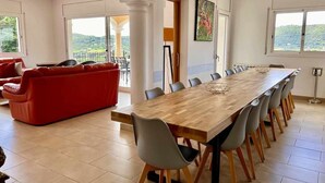A spacious dining area with a long wooden table and grey chairs, a red sofa, and a view of the outdoors. - Mas Ambros House with infinity pool and barbecues in Calonge, Girona Costa Brava (Calonge)