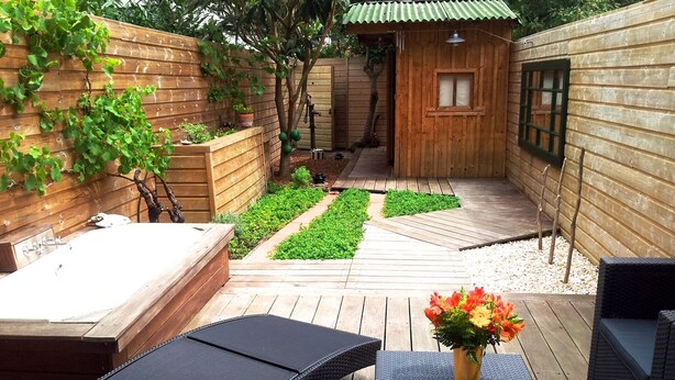 Eine Holzterrasse mit Whirlpool, Liegestühlen und einem kleinen Tisch mit Blumen in einer Vase.