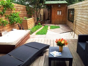 Une terrasse en bois avec un jacuzzi, des chaises longues et une petite table agrémentée d’un vase de fleurs.