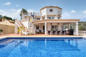 Una casa grande con piscina, mobiliario exterior y un patio cubierto.